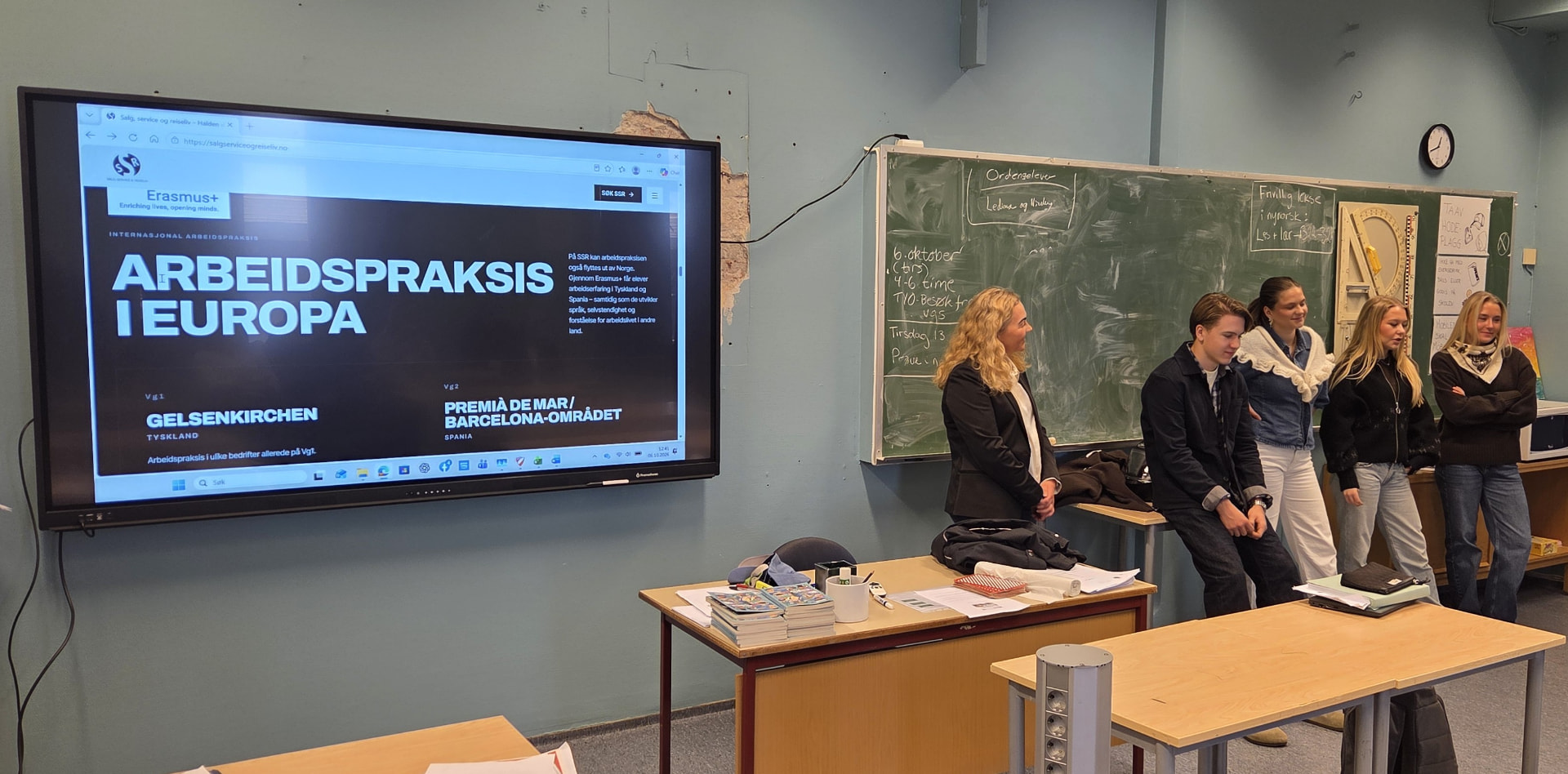 Vg2-elever og en lærer presenterer Salg, service og reiseliv i et klasserom, med nettsiden salgserviceogreiseliv.no vist på skjermen