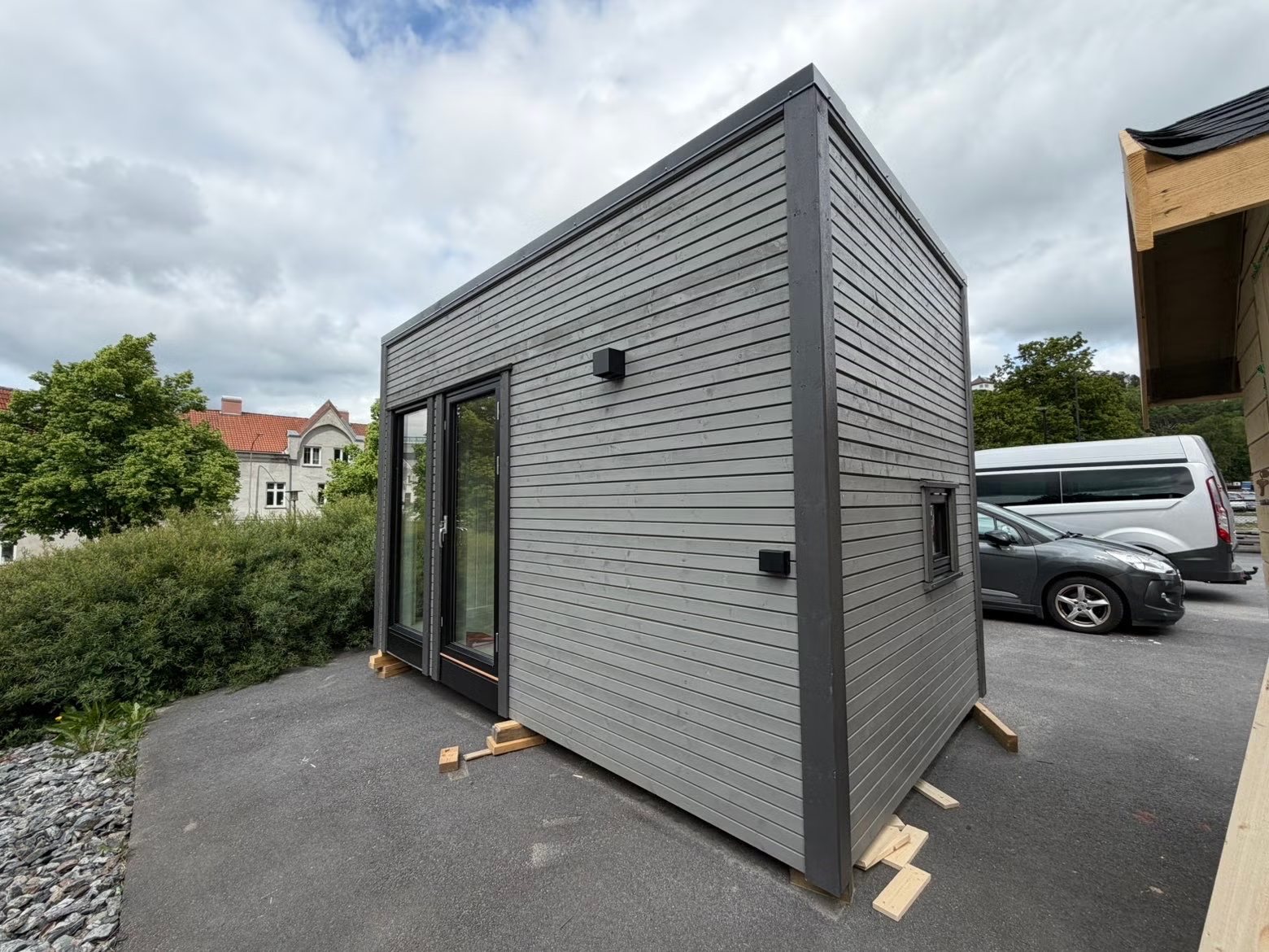 Elevbygget anneks med grå liggende kledning, sorte detaljer og glassdør.